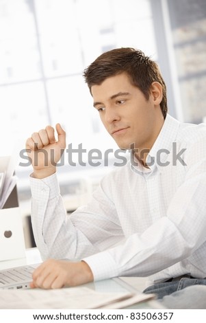 Young businessman sitting at office desk with laptop computer, thinking.?