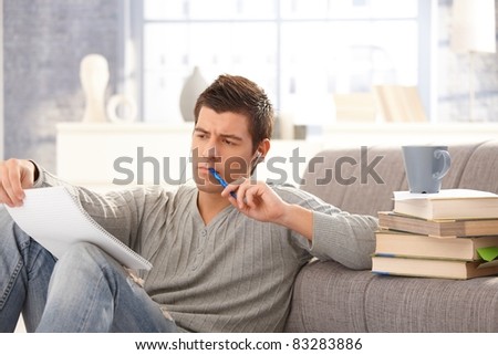 University student learning at home, holding notes and pen, listening to music.?
