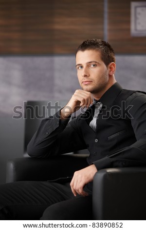 Handsome businessman waiting in office lobby, sitting in armchair.?