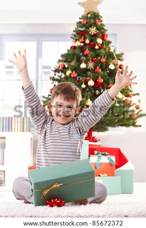 Happy kid sitting in pyjama on christmas morning, raising arms, getting christmas gift, laughing at camera.?