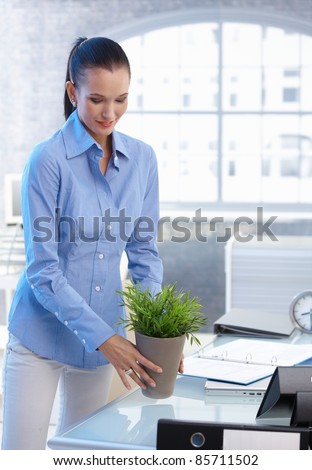 Smiling office worker girl moving plant pot from table.?