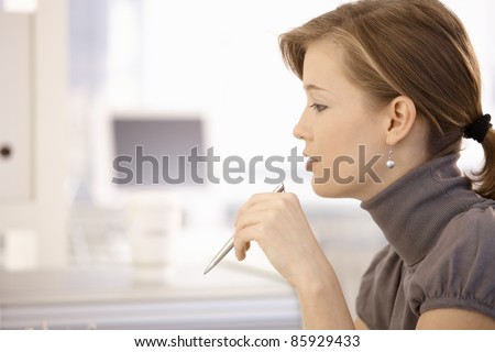 Closeup portrait of attractive young woman holding pen. Side view.?