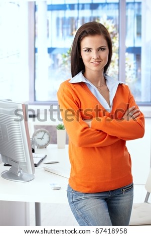 Young female office worker smiling arms crossed in bright office.?