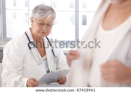 Senior female doctor looking at papers, sitting at desk.?