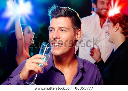 Young man drinking champagne at a party, people dancing at background.?