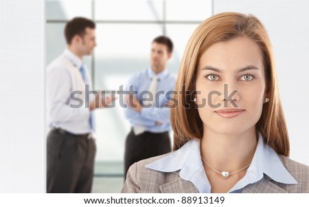 Portrait of attractive, smiling businesswoman, colleagues chatting in background.?