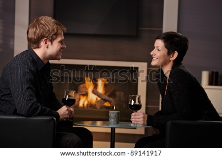 Young romantic couple dating, sitting in front of fireplace at home, drinking red wine.?
