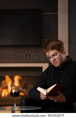 Young man sitting in front of fireplace at home on a cold winter day, reading book.?