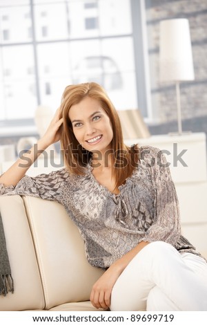Happy young woman sitting on couch in bright living room, laughing.?
