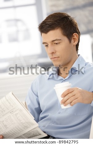 Young businessman on coffee break reading papers in office.?
