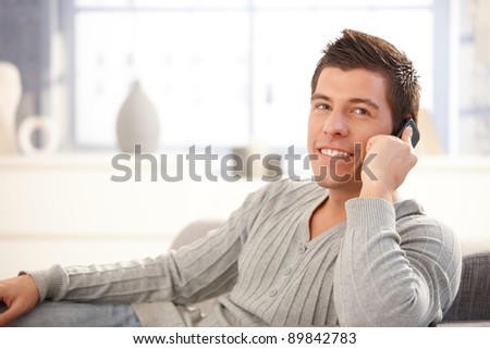 Happy young man speaking on mobile phone, smiling, sitting at home.?