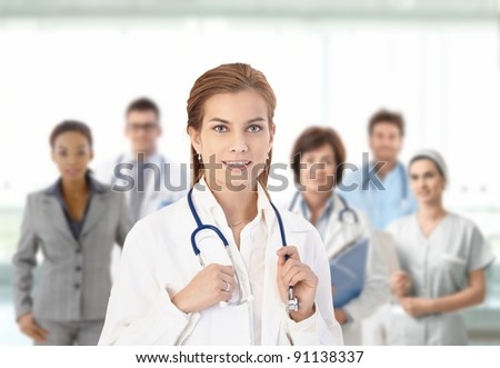 Young female doctor looking at camera, smiling, in front of medical team.?