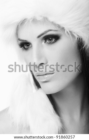 Beauty portrait of attractive young woman wearing white fur cap, looking away. Black and white photo.?