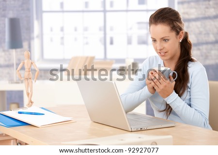 Attractive woman browsing internet at home, drinking tea, looking at screen.?