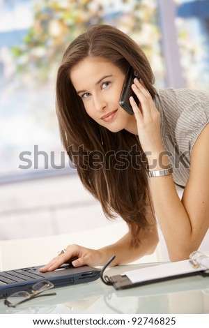 Portrait of working businesswoman, using laptop, on mobile phone call, smiling at camera.?