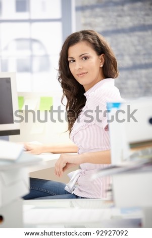 Young secretary working on computer in bright office, smiling.?