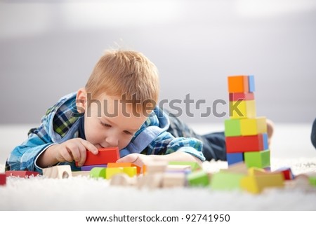 Cute 3 year old laying on floor, lost in playing with building cubes.?