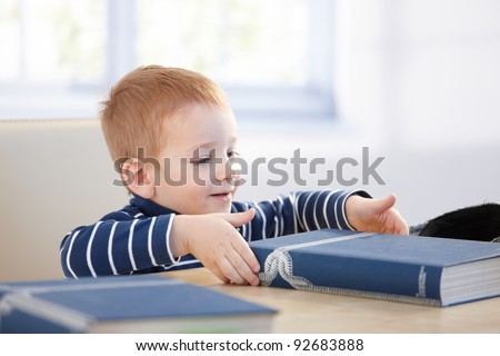 Ginger-haired little boy looking at encyclopedia at table, smiling.?