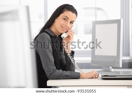 Pretty office girl at work, using landline phone, smiling at camera.?