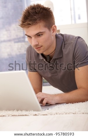 Young man lying on living room floor using laptop computer at home.?