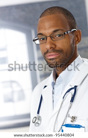 Closeup portrait of handsome afro medical doctor wearing smock, looking at camera.?
