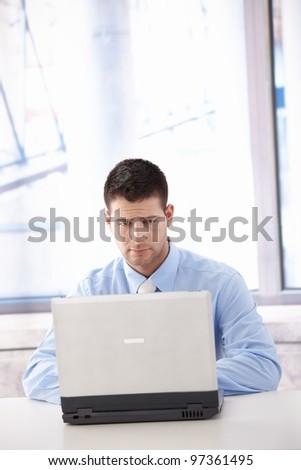 Young businessman working on laptop, looking at screen troubled.?