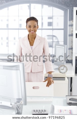 Happy businesswoman standing at desk in bright office, smiling at camera.?