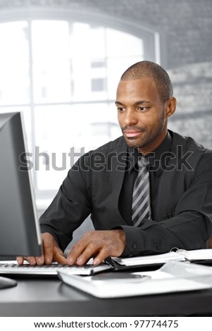 Elegant afro businessman concentrating on working on computer at office desk.