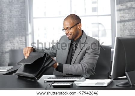 Businessman sitting at office desk searching in briefcase.