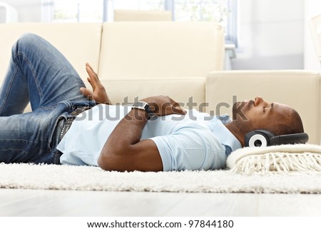 Leisure with music, ethnic man lying on living room floor with headset, enjoying with closed eyes.