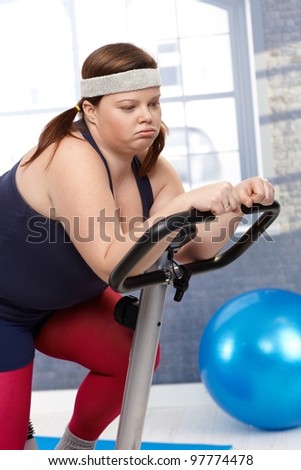 Exhausted fat woman sitting on exercise bike after workout.