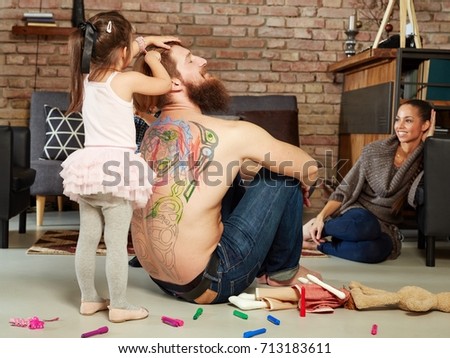 Little girl playing with father at home, combing his hair, colouring his back.