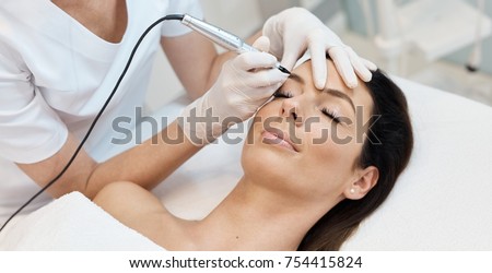 Beautiful woman having professional eyebrow tattoo in beauty salon.