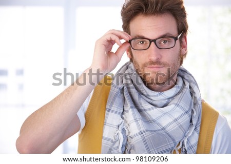 Young man standing front of window in living room, wearing glasses, looking at camera.
