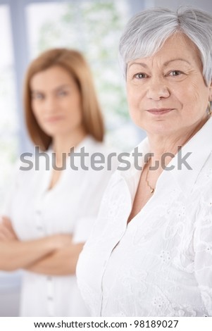 Portrait of elderly woman smiling, young woman standing at background.