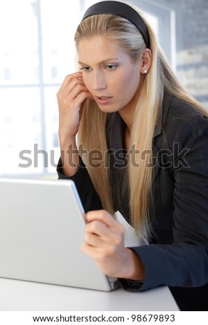Blonde assistant girl looking at laptop computer, concentrating.