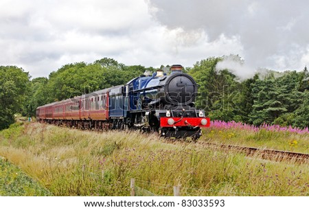 Summer trips in steam. Large blue steam train on a day trip with passengers through a summer scene
