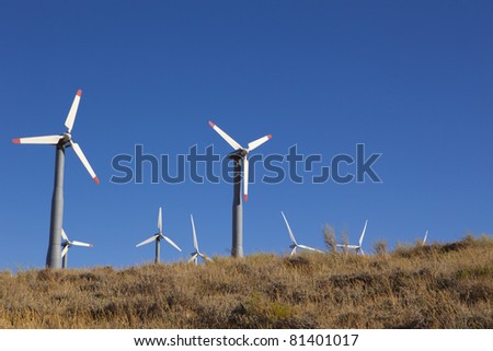 A wind farm of turbines sits on top of a hillside.