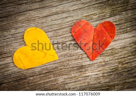 Yellow and red autumn leaves in love heart shape with wooden background.