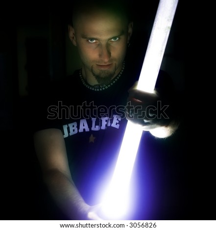A man holds a long, glowing Star Wars light stick in his hands in the dark.