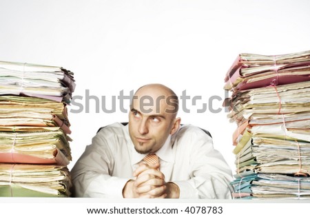 Young adult man sits between 2 large stacks of file folders. He has a smirking expression on his face.