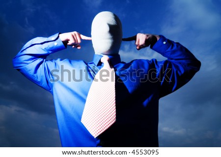Man in blue shirt and necktie, face and head wrapped,fingers pointing at ears, blue sky background