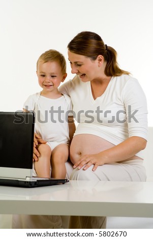 A pregnant mother with her child sitting on her knee looking at a laptop computer. Both are smiling.