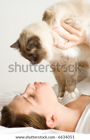 Lady playing with cat in bed. Wearing casual white attire.