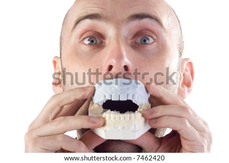 A closeup of a man, raising his eyebrows and playfully holding a model of his mouth to his mouth.