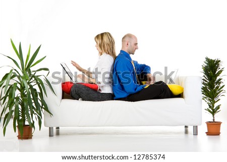 A male and female business executive sitting on a sofa back to back with their laptops