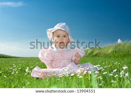 Beautiful baby girl wearing bonnet sat in field of flowers under blue sky.