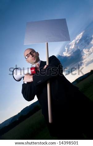 Serious bold man in glasses and black suit, holding sign and megaphone. Space for text is available.