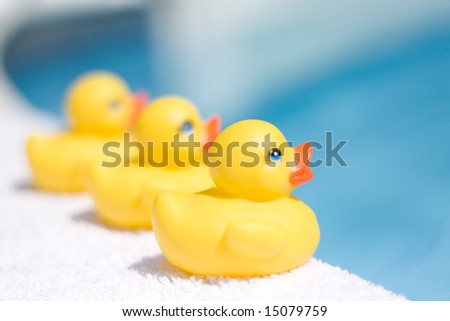 Three yellow toy ducks on a white towel besides a swimming pool depicting summer season.