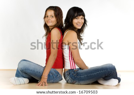 Two smiling teenage girls sitting back-to-back on the floor, caucasian/white.